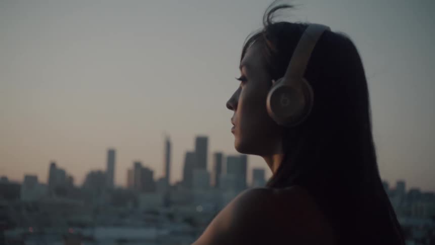 A woman is leaning against a railing overlooking a city at sunset