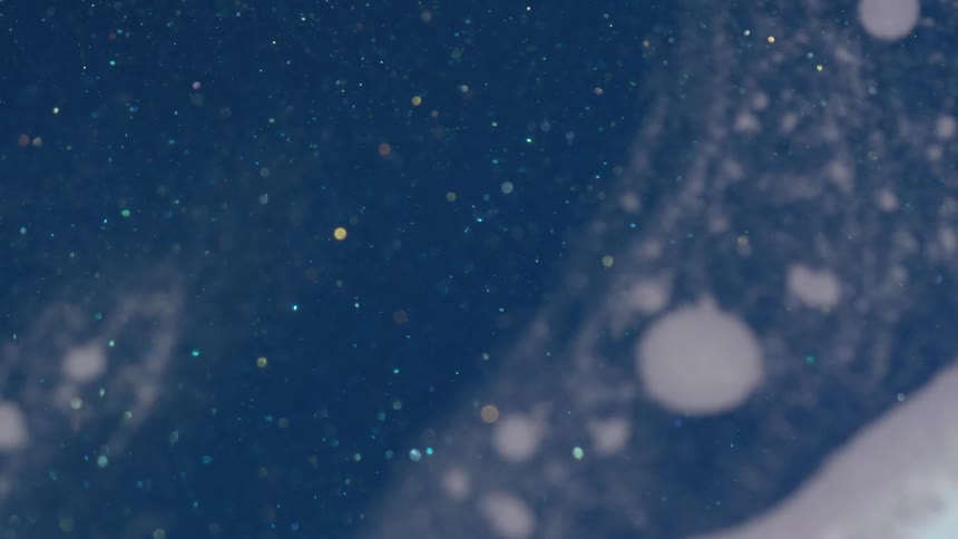 Small pieces of iridescent glitter float across blue and white background