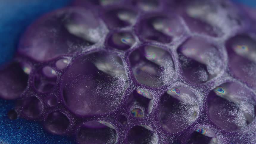 Atop a viscous purple liquid with glitter particles suspended in it are a cluster of bubbles