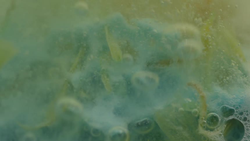 Bubbles rise and foam around blue and yellow pastel material