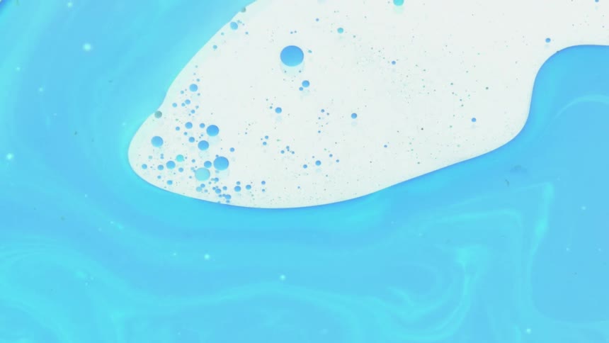 Blue liquid flows and ebbs leaving bubbles and scatter remnants against clear surface
