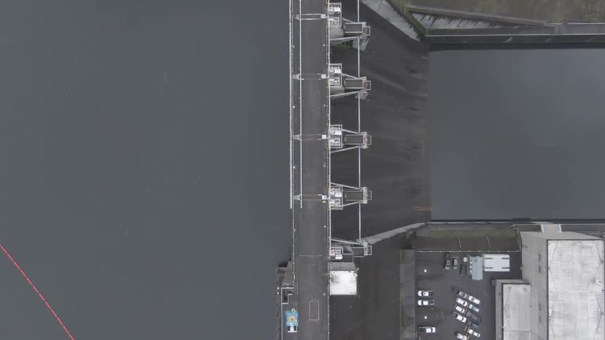 A dam with water with a person walking and vehicles