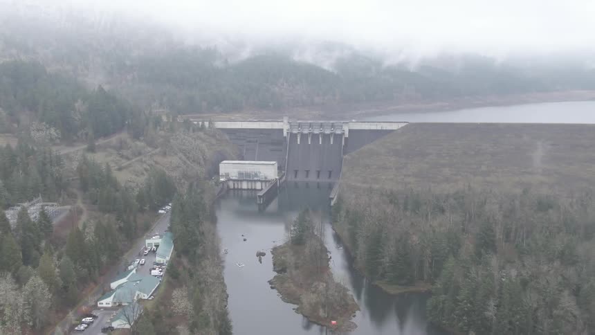 Thick fog sets over a river and dam near a boathouse