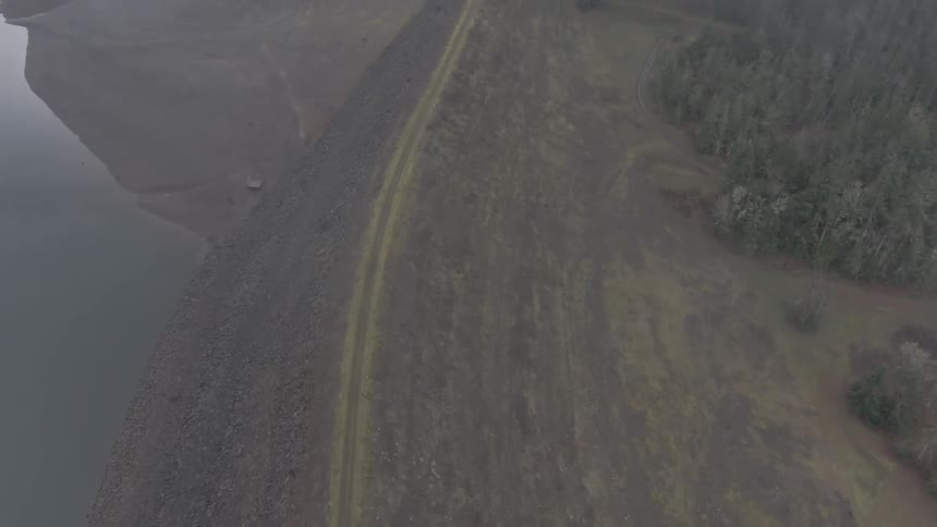 Fog obscures water road bordered by steep slope and forest