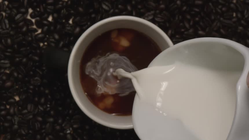 Creamer or milk is poured into a mug of coffee