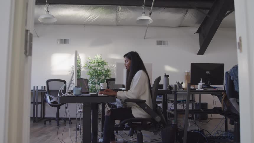 A young black woman types on a keyboard while sitting at a desk in an open office
