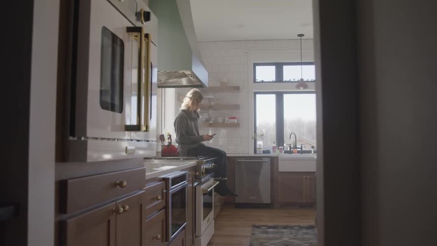 A person sitting on a kitchen counter texting on a phone