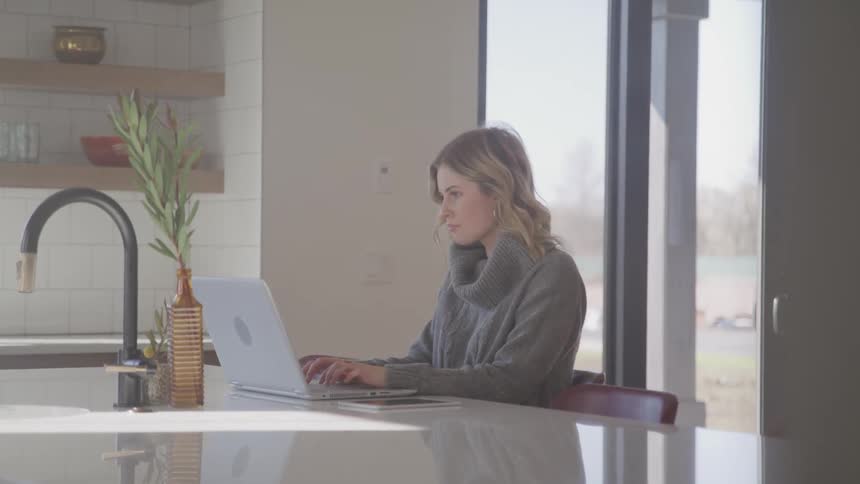 A woman sits at a kitchen island with a laptop
