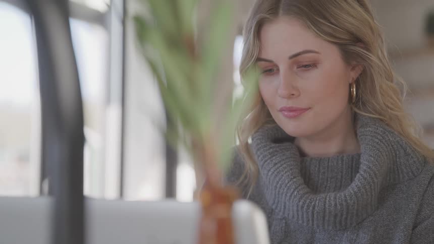 Woman wearing a gray knitted sweater looks at a white laptop