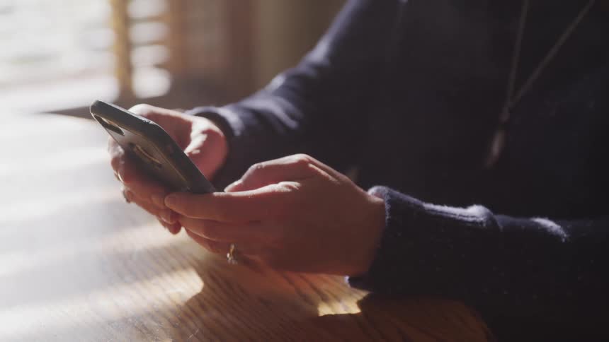 A woman holds a smart phone and types a message into it