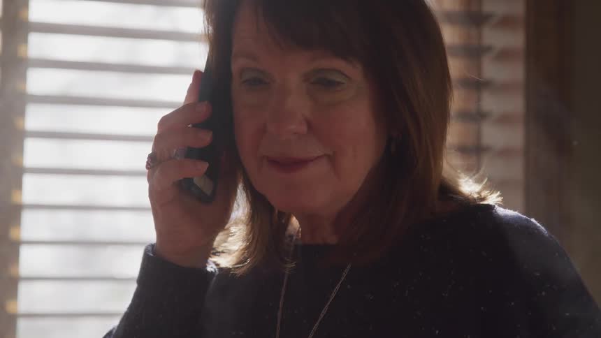 Woman talks on a smartphone near a window in a room at home