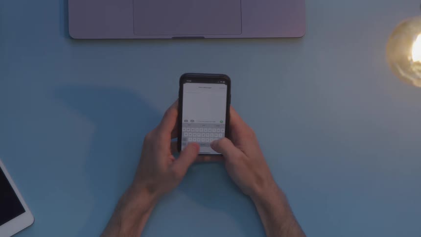 A person rests their arms on a table to type on a smartphone before pulling their arms back out of frame