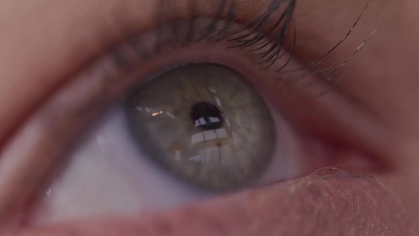 A person with green eyesblinks as they are looking upwards