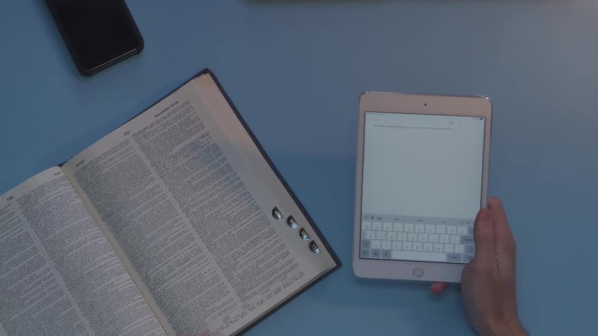 A person flipping through a book and typing on a tablet