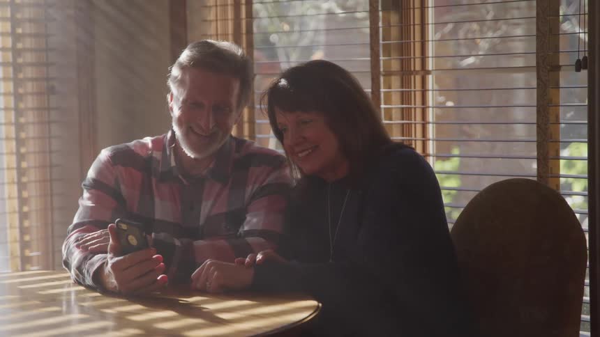 Couple uses a phone for a video call sitting on a table at home