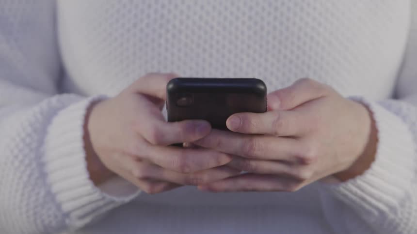 Woman with a white knitted sweater uses a smartphone