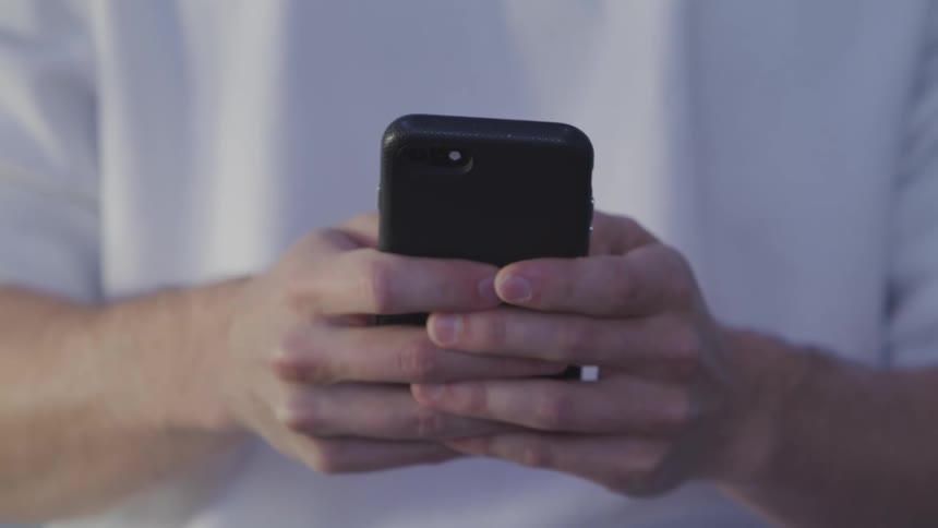 Man standing outdoors types a number on his smartphone to make a call