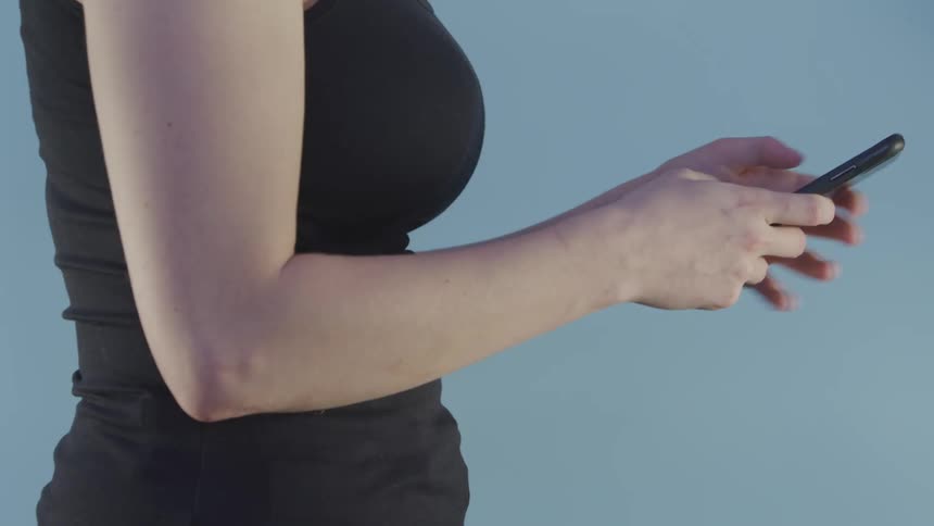 A young woman scrolls on her cell phone and then lifts it towards her head