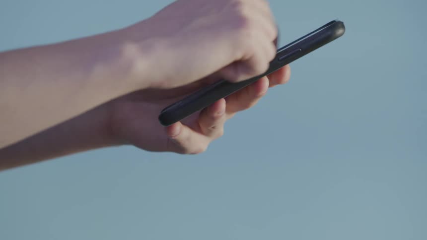 Mans hands uses a smartphone in front of a blue wall