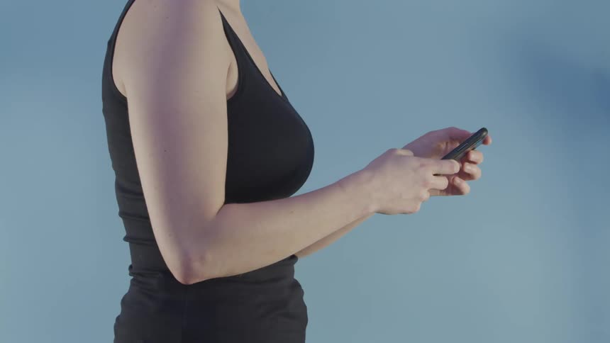 A woman in a tank top types on her smartphone before raising the phone to her ear