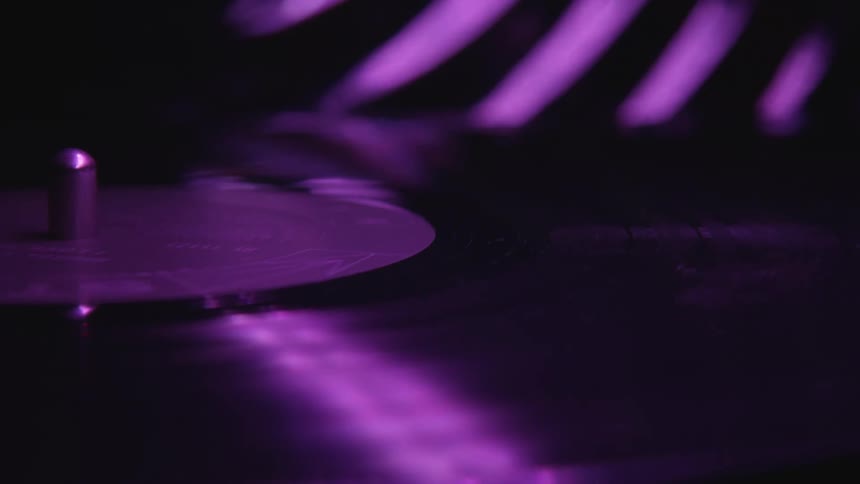 Vinyl record spinning on a turntable reflecting purple lights