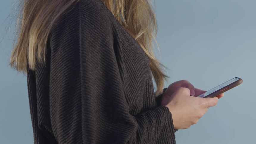 Blonde woman wearing sweater texts on mobile phone before making call