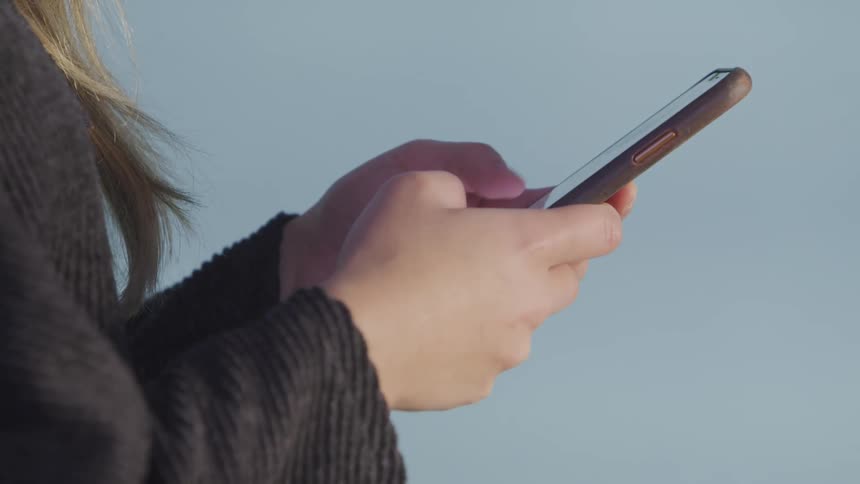 A young female types a message quickly on her smartphone before holding it up to her ear