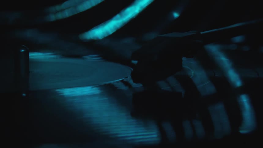 Vinyl record spinning under a needle reflects the blue lights of a dimly lit room