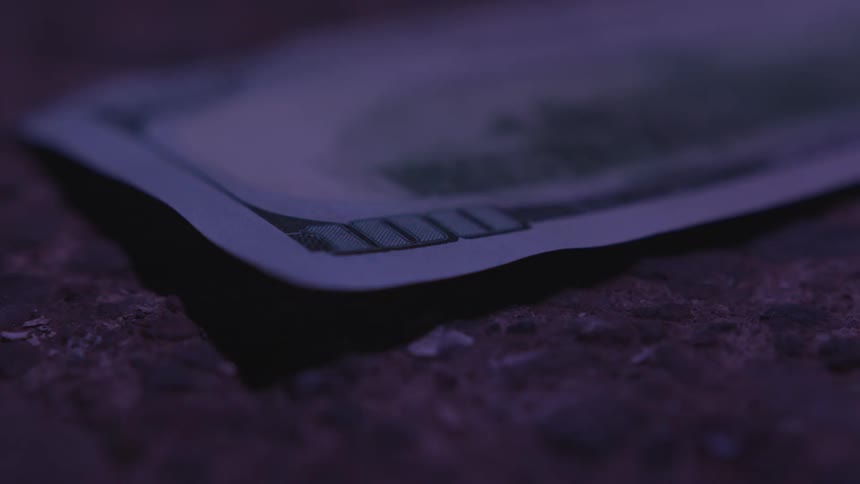 A hundred dollar bill on the ground with light and shadow