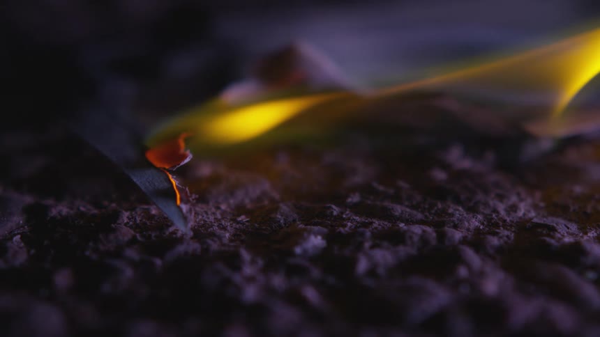 Yellow flames consume a piece of paper burning on the ground
