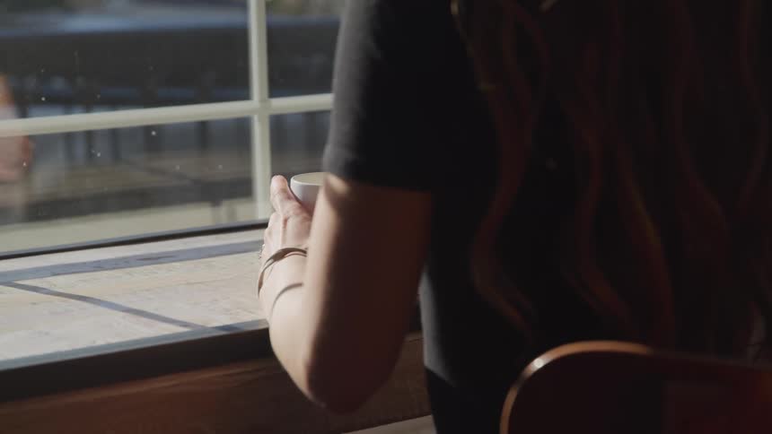 A woman sits near a window holding a cup