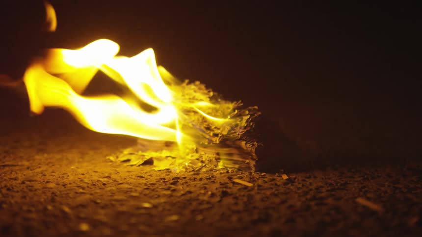 A orange yellow fire burns amongst an small object on the ground under the night sky