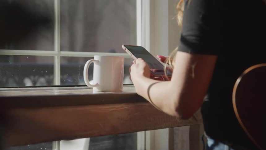 A woman sits in a restaurant with a cup of coffee and scrolls on her cell phone