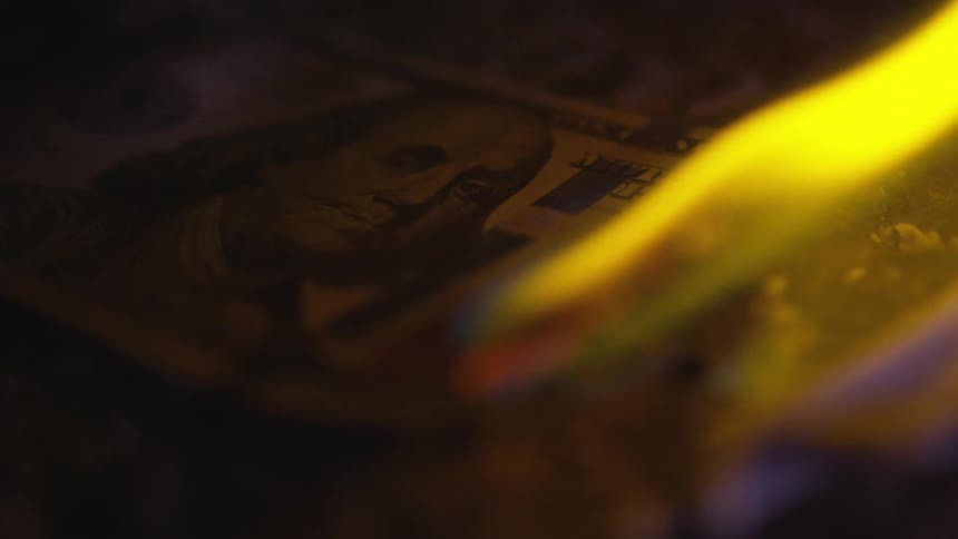 One hundred dollar bill burns yellow lighting up shadows