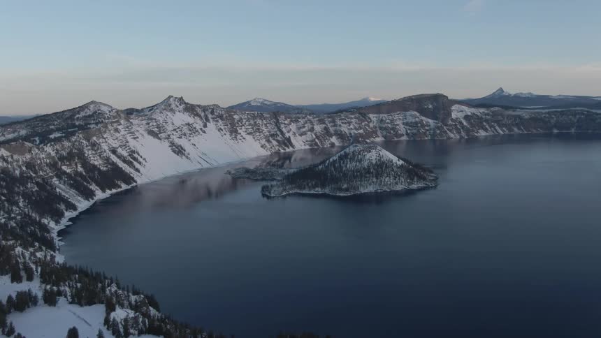 Small island in a crater lake on the snow covered mountain range