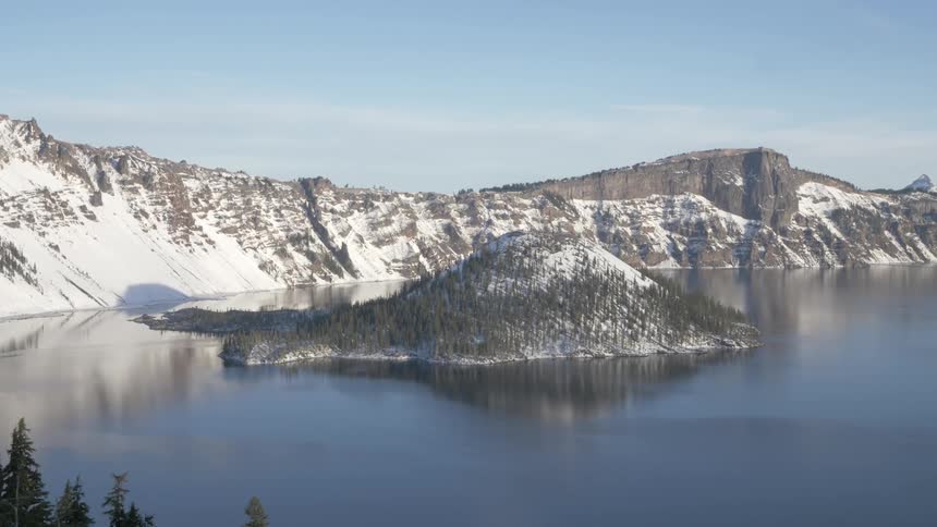 A layer of ice covers a still lake at the base of a canyon