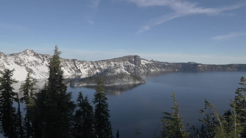 Placid waters of a lake reflecting the snow covered mountain range near the pine tree forest