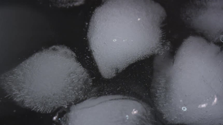 Ice cubes collide into each other as carbonation and bubbles rise to the surface of a beverage
