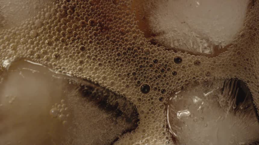 A soda with bubbles ice and fizz with the light reflecting off of it