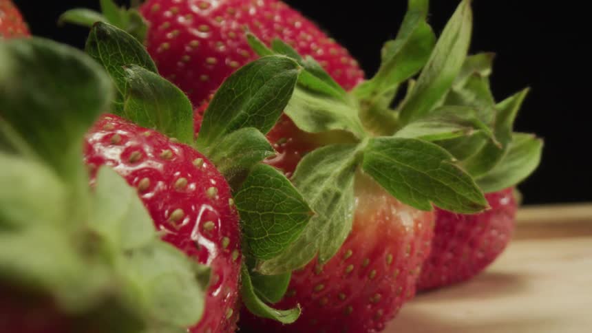 Close up of a pile of red strawberries with green leafs on a table