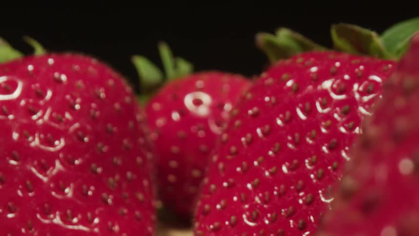 Rows of shiny red strawberries sitting on pale surface contrasting with black background