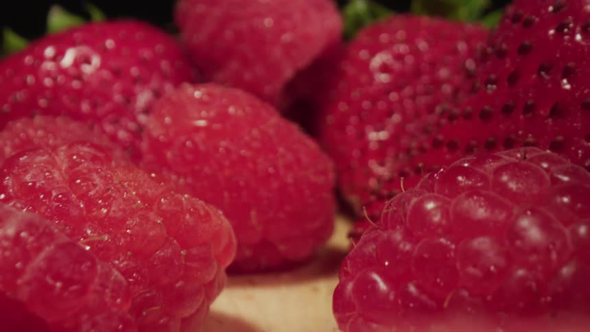 Red juicy strawberries and raspberries sitting on a wood table