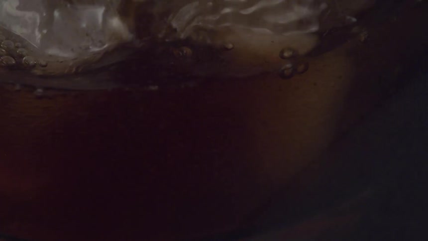 A brownish beverage is poured into a glass over several cubes of ice