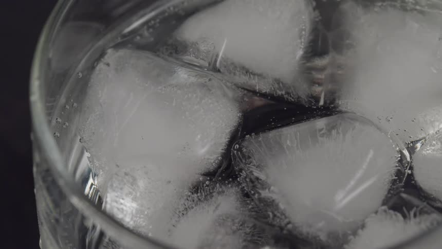 A glass with ice water and bubbles with light reflecting off of it