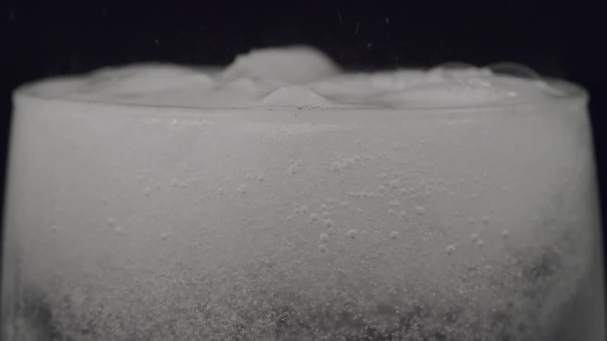 Clear soda water is added to ice cubes in glass causing foaming
