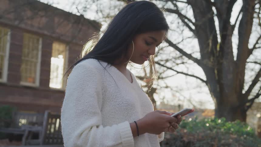 A woman stands outside of a building looking at her cell phone