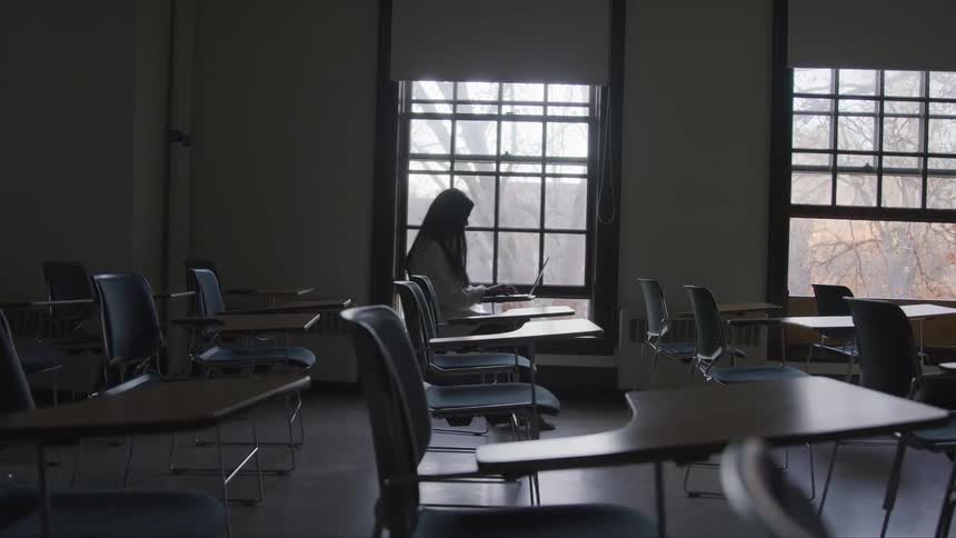 A female sits in a dark classroom with a laptop