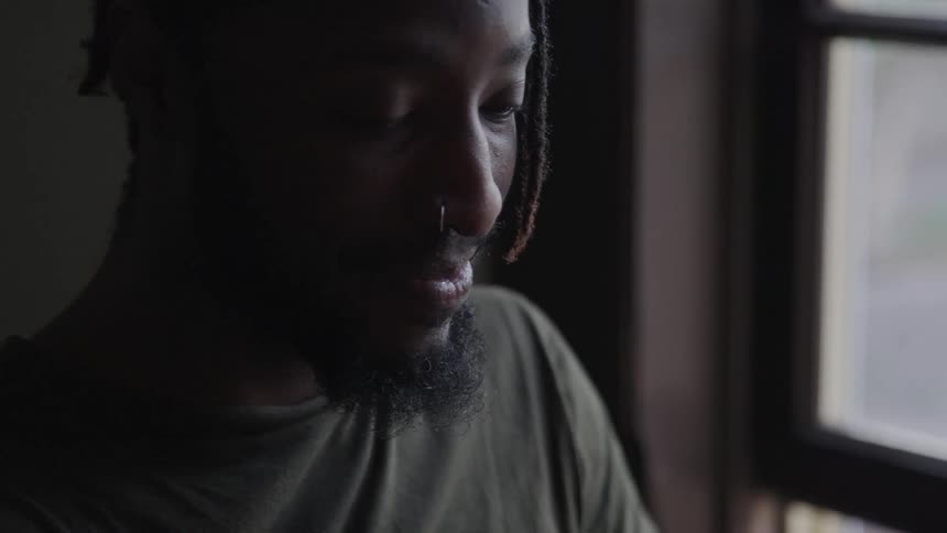 A man with a nose ring sitting in a room next to a window