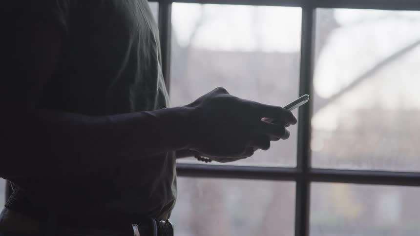 A man standing next to a window holding a smart phone