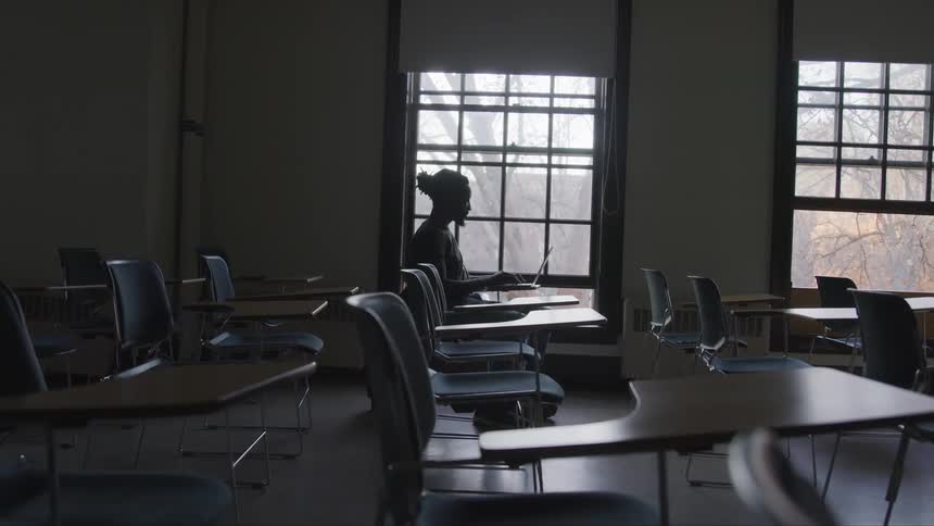 Man sits at desk typing on laptop near window showing leafless trees